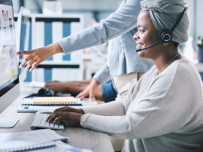 African american call centre telemarketing agent receiving training and assistance from supervisor .