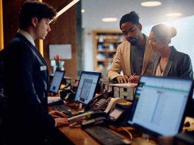 Happy woman and her African American husband filing registration paperwork at hotel reception desk.